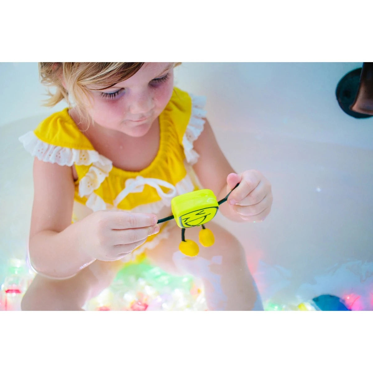 Criança brincando com o GloPals Alex amarelo na banheira, um brinquedo sensorial luminoso.