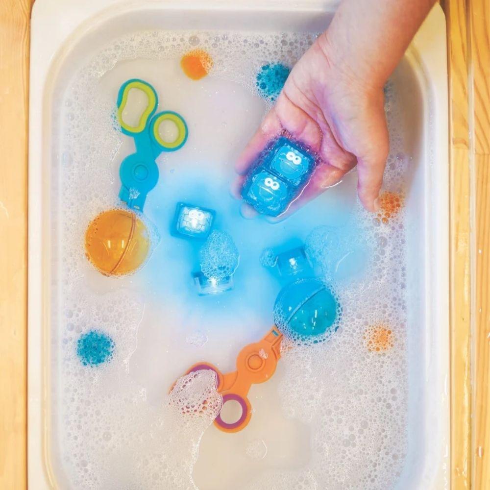 Mesa sensorial com água e diversos brinquedos, incluindo os cubos de luz GloPals Monstro das Bolachas a brilhar.