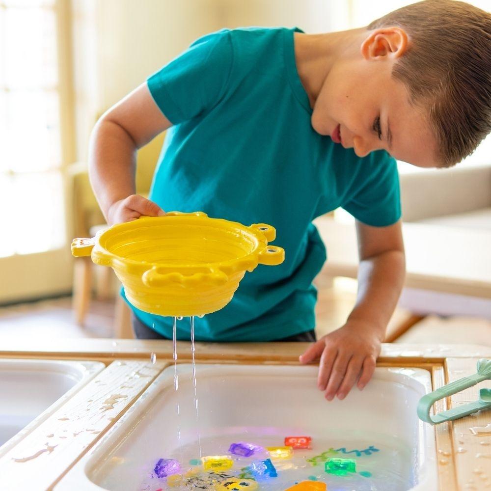 Menino a usar filtro GloPals amarelo para coar água de brincadeira sensorial.