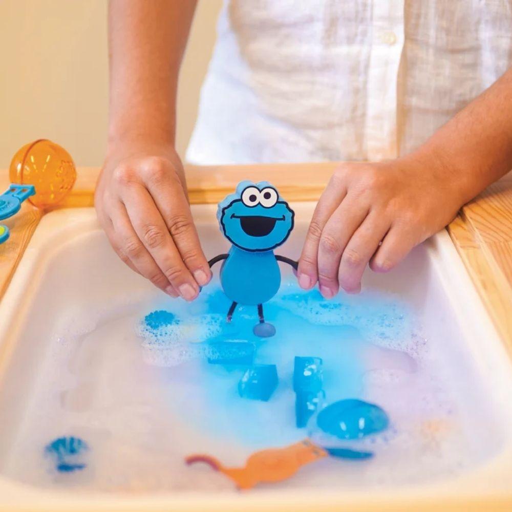 Criança a brincar com o Monstro das Bolachas GloPals e cubos de luz numa mesa sensorial com água, mostrando a interação lúdica.