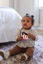 Bebé sentado no tapete a segurar o GloPals Mordedor & Guizo com luz Lilás, que brilha em roxo, demonstrando a sua pega ergonómica.