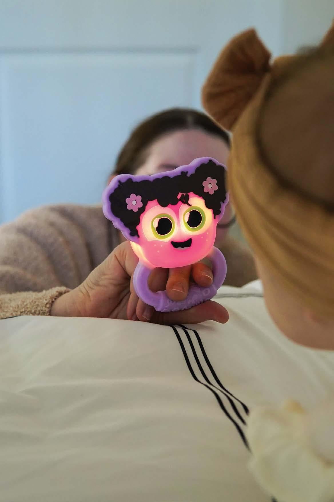 GloPals Mordedor & Guizo com luz Lilás, a brilhar em roxo, segurado por um adulto para um bebé, realçando a sua funcionalidade luminosa.