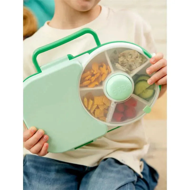 Criança segura lancheira GoBe Snack Spin 2 em 1 verde com lanches variados no dispensador giratório.