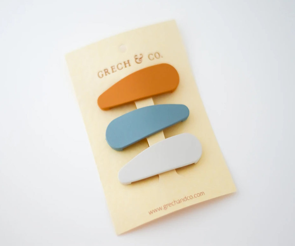 Conjunto de 3 ganchos de cabelo Grech & Co. em tons mate (laranja queimado, azul claro e cinza claro) apresentados na embalagem de cartão bege.