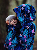 Camisola Greyse 5 em 1 para babywearing em azul Monstera, usada por uma mulher grávida, demonstrando o uso de casaco casual.