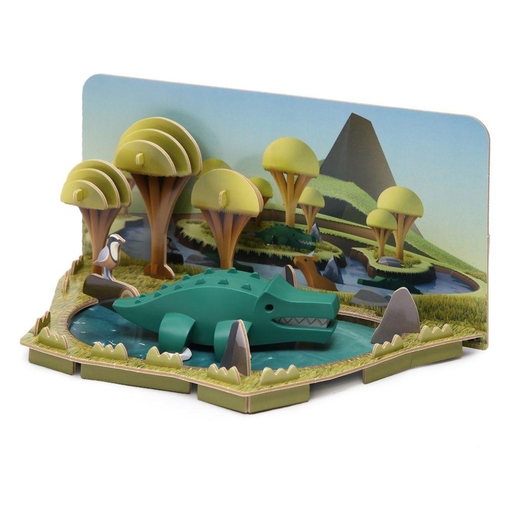 Crocodilo de brincar Halftoys montado no seu diorama 3D, mostrando o habitat natural com árvores e água.