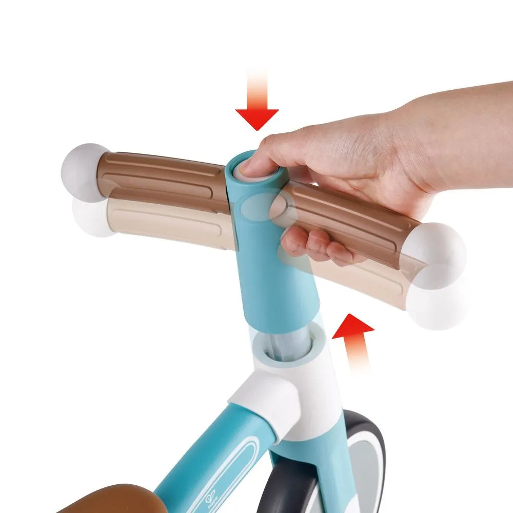 Detalhe do ajuste de altura do guiador da bicicleta de equilíbrio Hape, com mão a pressionar o botão de ajuste.