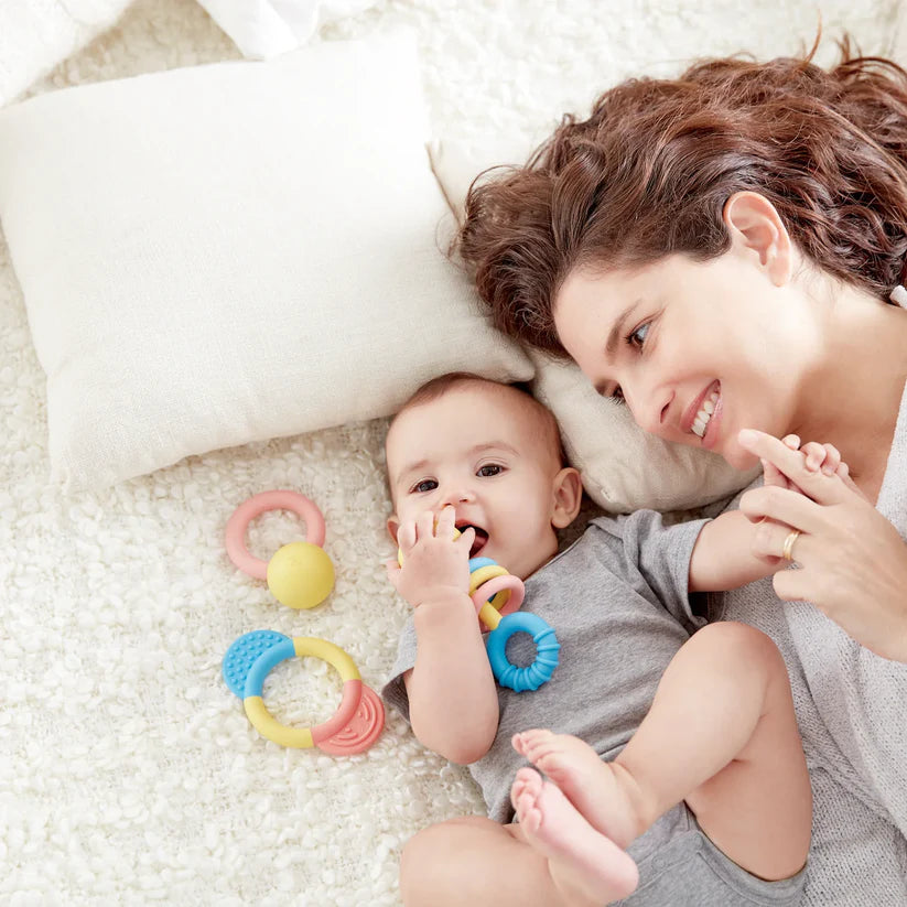 Mãe sorridente a interagir com o bebé que está a morder um dos mordedores Hape, momento de conforto e dentição.
