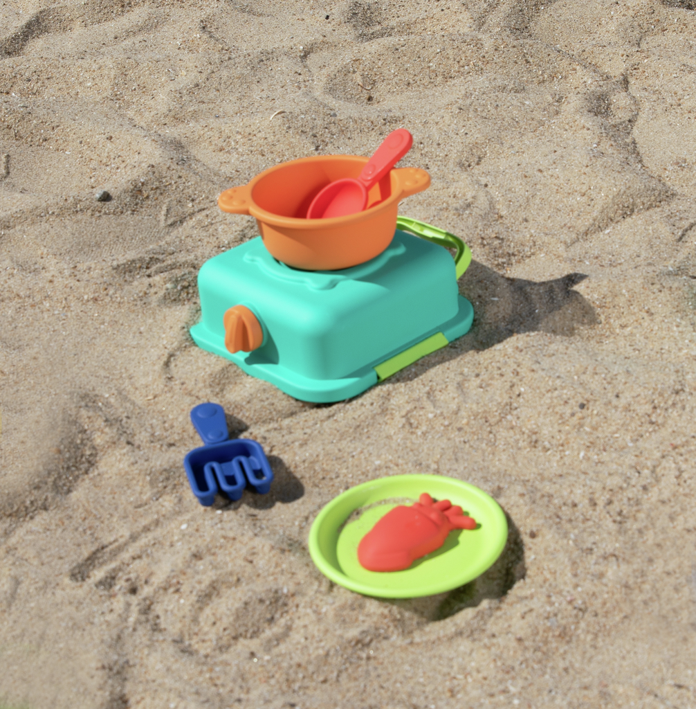 Utensílios de cozinha Hape dispostos na areia da praia prontos a brincar.
