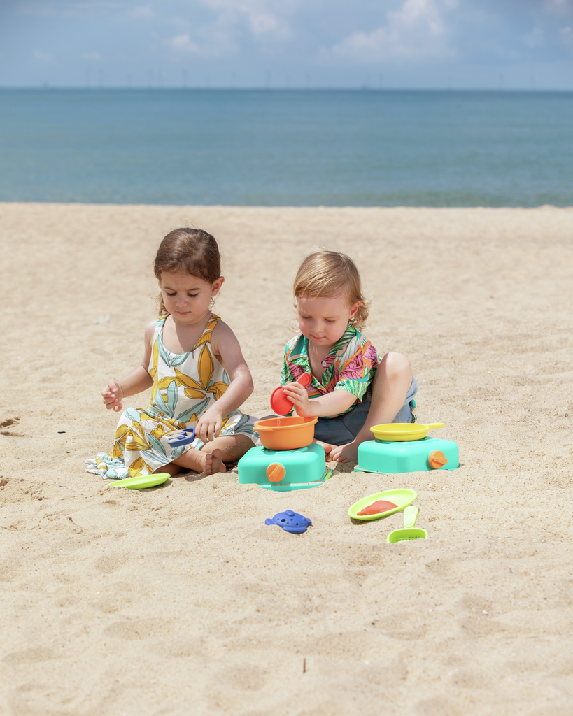 Duas crianças a preparar receitas de areia com o kit de cozinha Hape na praia.