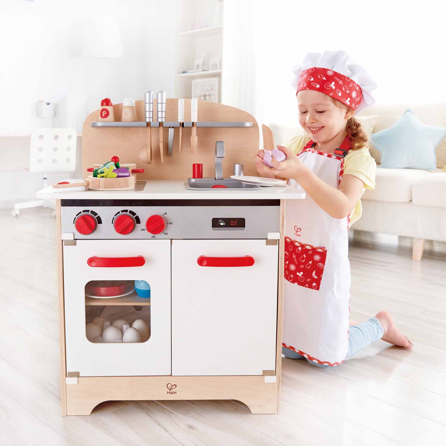 Menina com o Hape Fato de Chef pastelaria a brincar numa cozinha de faz de conta.
