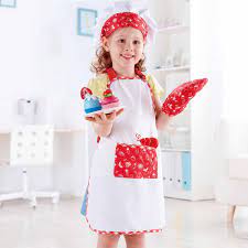 Menina sorridente a usar o Hape Fato de Chef pastelaria, segurando cupcakes de brincar.