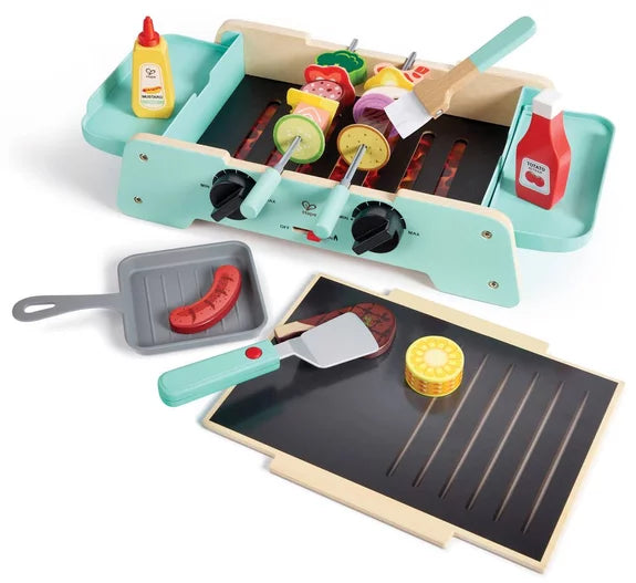 Conjunto de acessórios do Hape Grelhador: espetadas, bife, milho, frigideira e molhos de ketchup e mostarda junto à base.