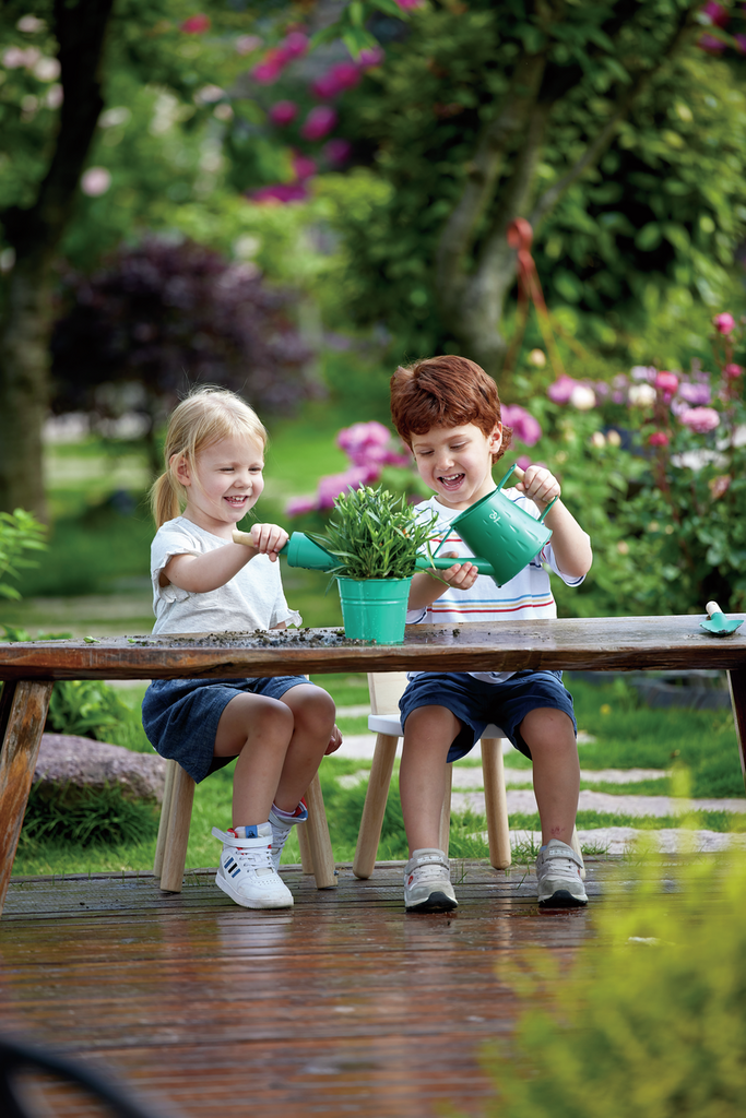 Duas crianças felizes a brincar com o conjunto de jardinagem Hape num jardim.