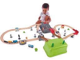 Criança a brincar com o Hape Kit Construção cidade e comboio 50 peças, montando o circuito e usando a caixa como cenário.