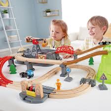 Duas crianças a brincar com o Hape Kit Construção cidade e comboio 50 peças, interagindo com a grua e o comboio.