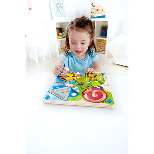 Criança pequena a brincar com o labirinto magnético Hape, desenvolvendo a motricidade fina na sala de estar.
