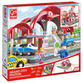 Caixa do Hape Mega Kit Construção cidade e estação comboios, mostrando a estação, comboio, táxi e figuras de brincar.