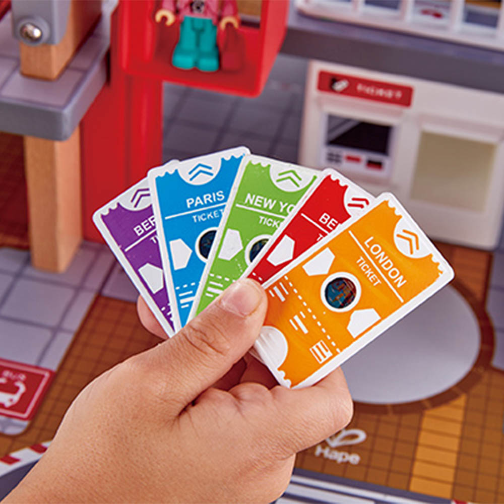 Mão a segurar um leque de cinco bilhetes de comboio coloridos (Paris, Nova Iorque, Londres, etc.) do set Hape.