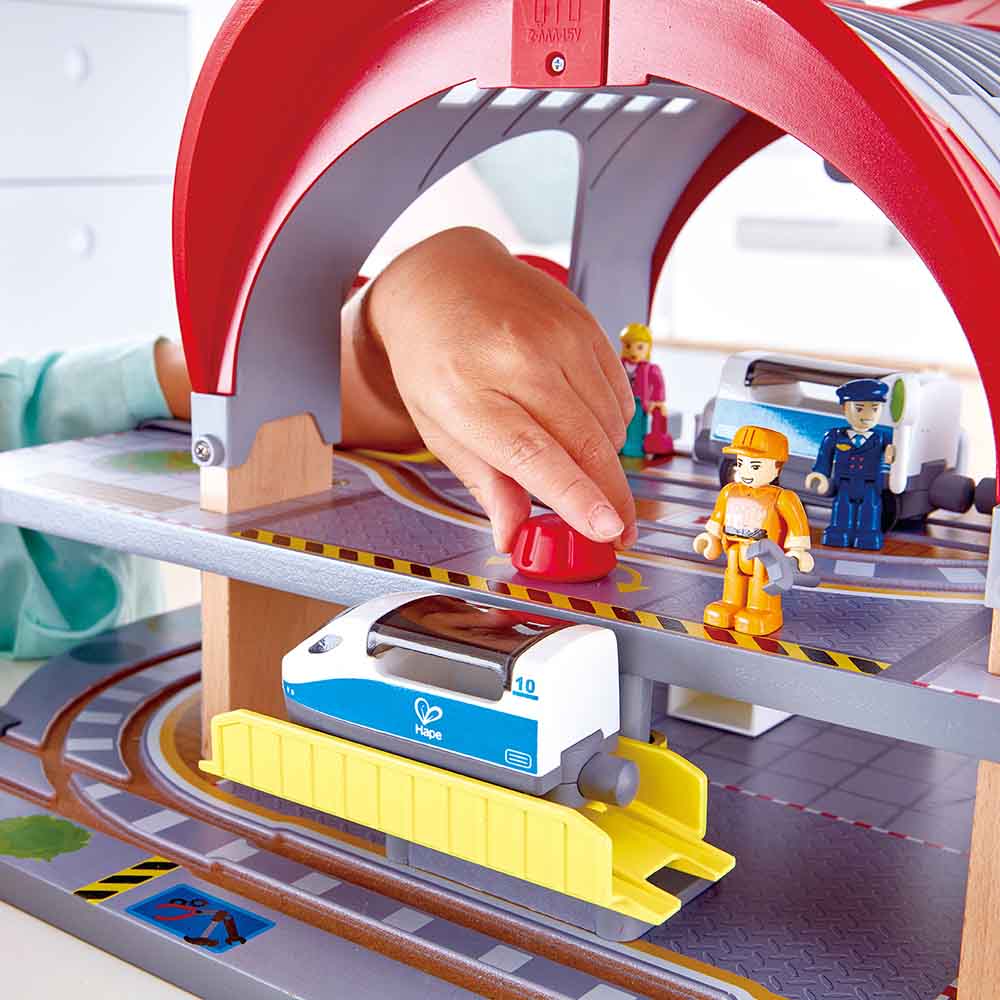 Criança brinca com o Hape Mega Kit comboios, interagindo com o elevador da estação e o comboio de alta velocidade.