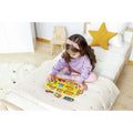 Criança pequena sentada numa cama a brincar com o puzzle de madeira Hape Veículos de Construção, encaixando as peças.