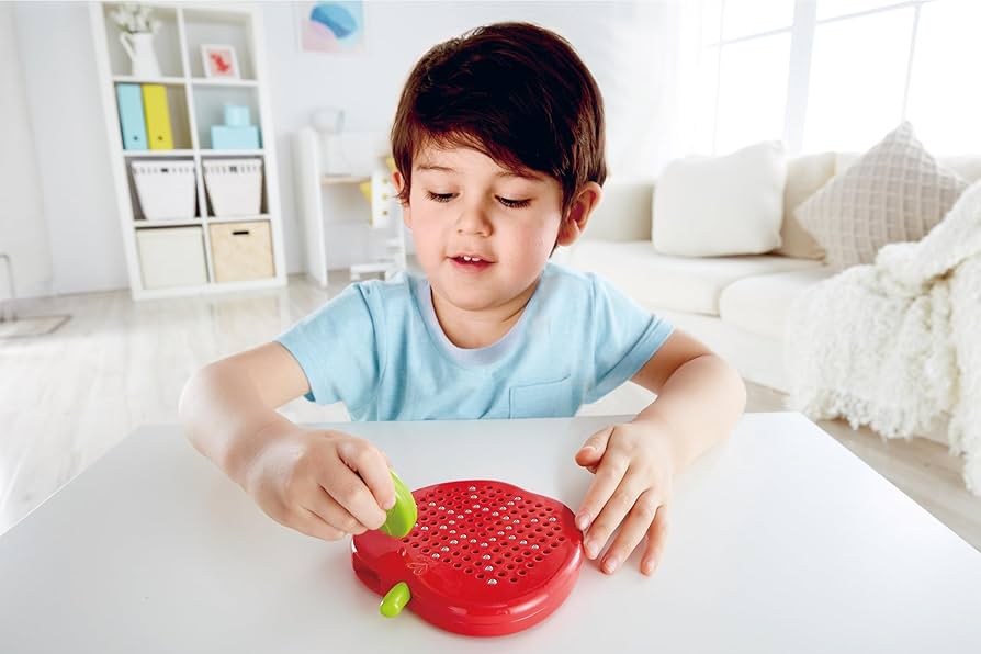 Menino a brincar com o quadro de desenho magnético Hape em forma de maçã, usando o íman folha para criar padrões.