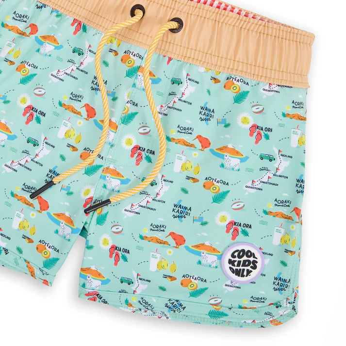 Detalhe em close-up dos calções de banho Hello Hossy, mostrando o padrão vibrante inspirado na Nova Zelândia e o logótipo "Cool Kids Only".