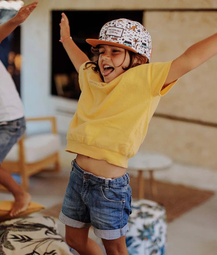 Criança salta feliz com boné Hello Hossy Aussie, mostrando conforto para brincar.