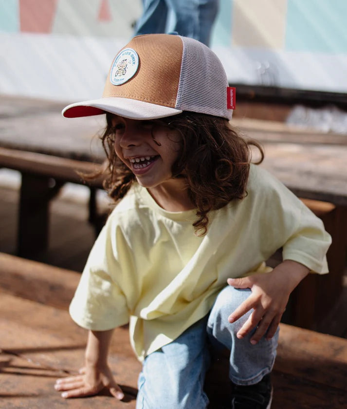 Criança feliz a usar o boné trucker Biker Hello Hossy com patch, sentada num banco.