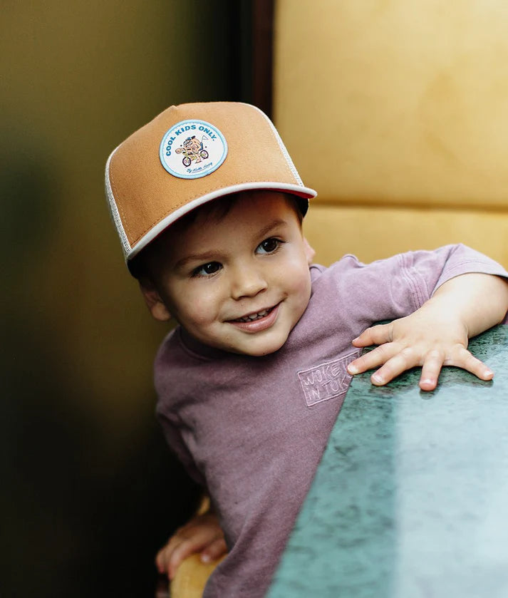 Menino com o boné Hello Hossy Biker, sorrindo, mostrando o patch "Cool Kids Only".