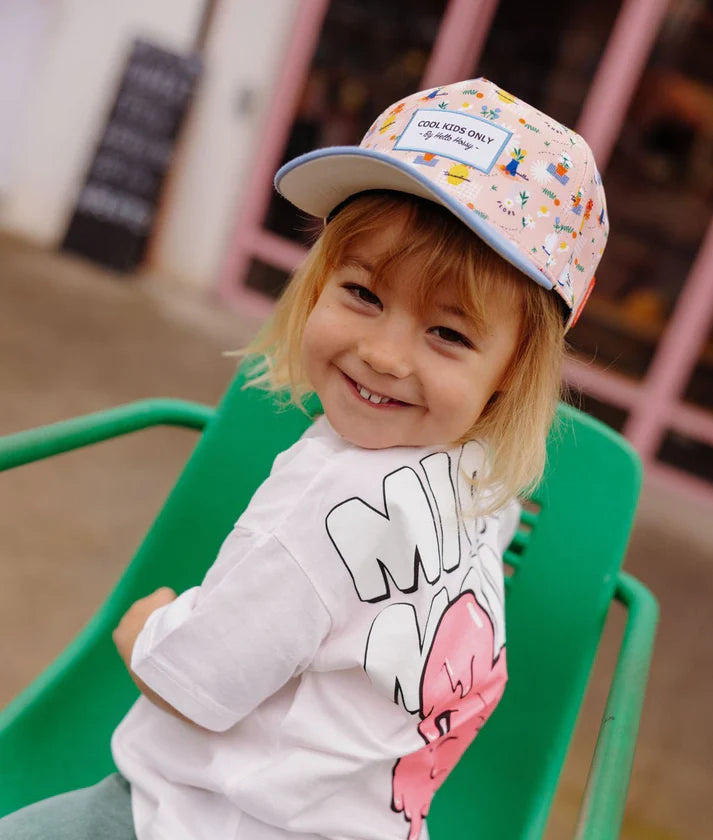Menina sorrindo usando o boné Flore Hello Hossy. Acessório infantil moderno e divertido com padrão floral.