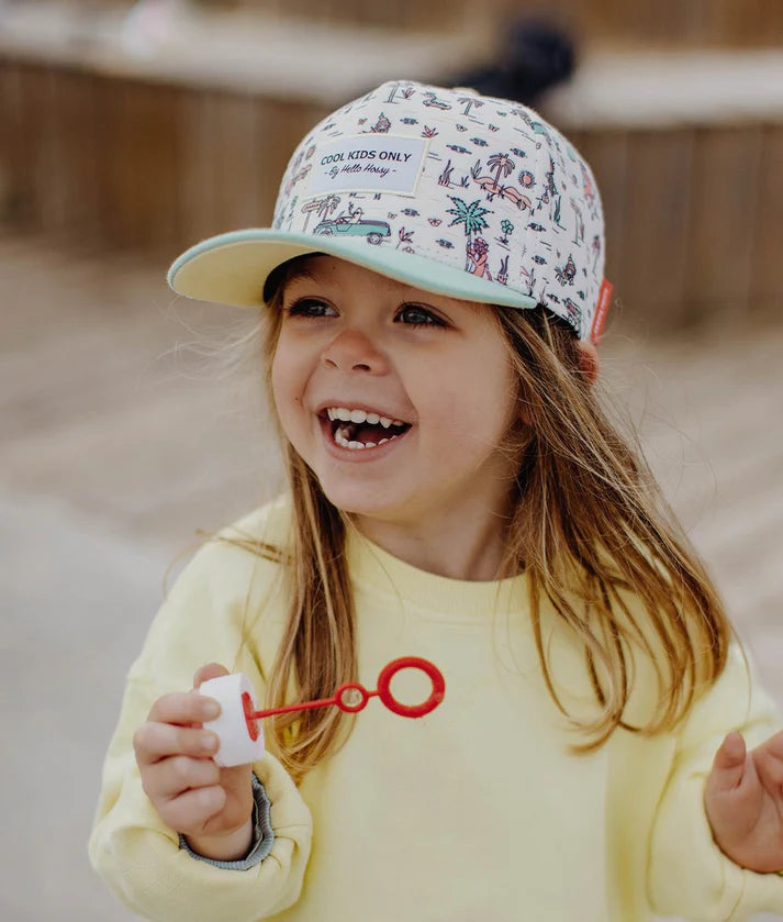 Menina feliz a usar boné Hello Hossy Jungly com estampado divertido, perfeito para aventuras ao ar livre.
