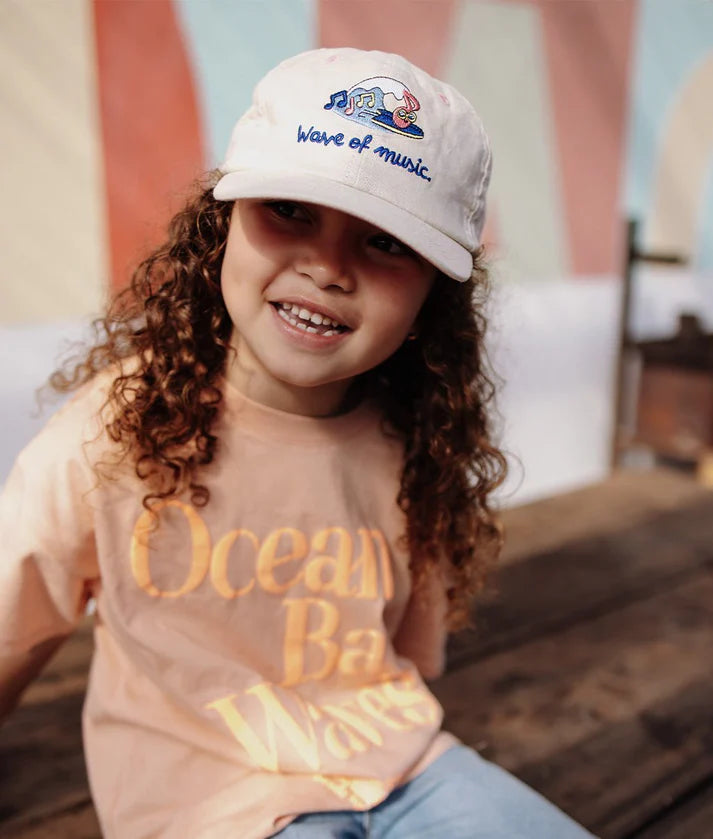 Menina feliz usa boné HELLO HOSSY Wave linho algodão. Design moderno e confortável para crianças.