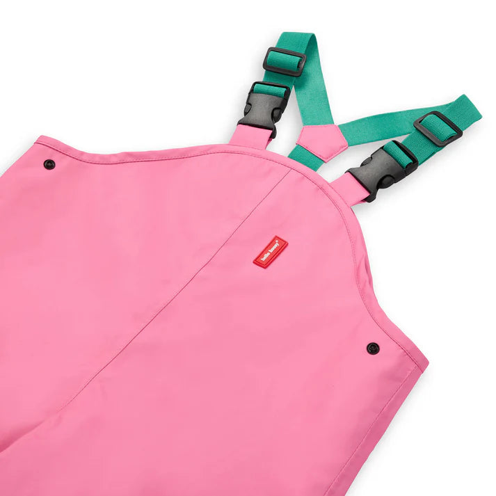 Detalhe superior do macacão rosa Hello Hossy, focando nas alças ajustáveis verdes com fivelas pretas e etiqueta da marca.