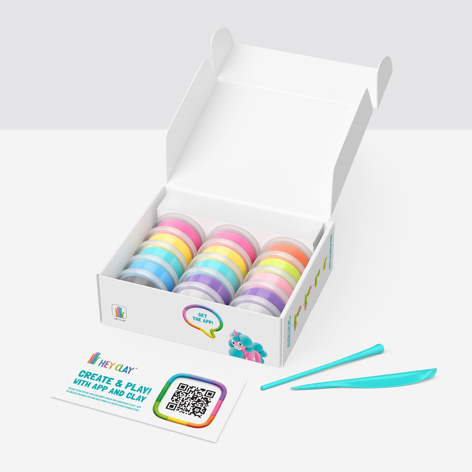 Interior da caixa HEY CLAY aberta, mostrando 15 latas de pasta de modelar colorida, duas ferramentas de escultura e um cartão com código QR para descarregar a aplicação.