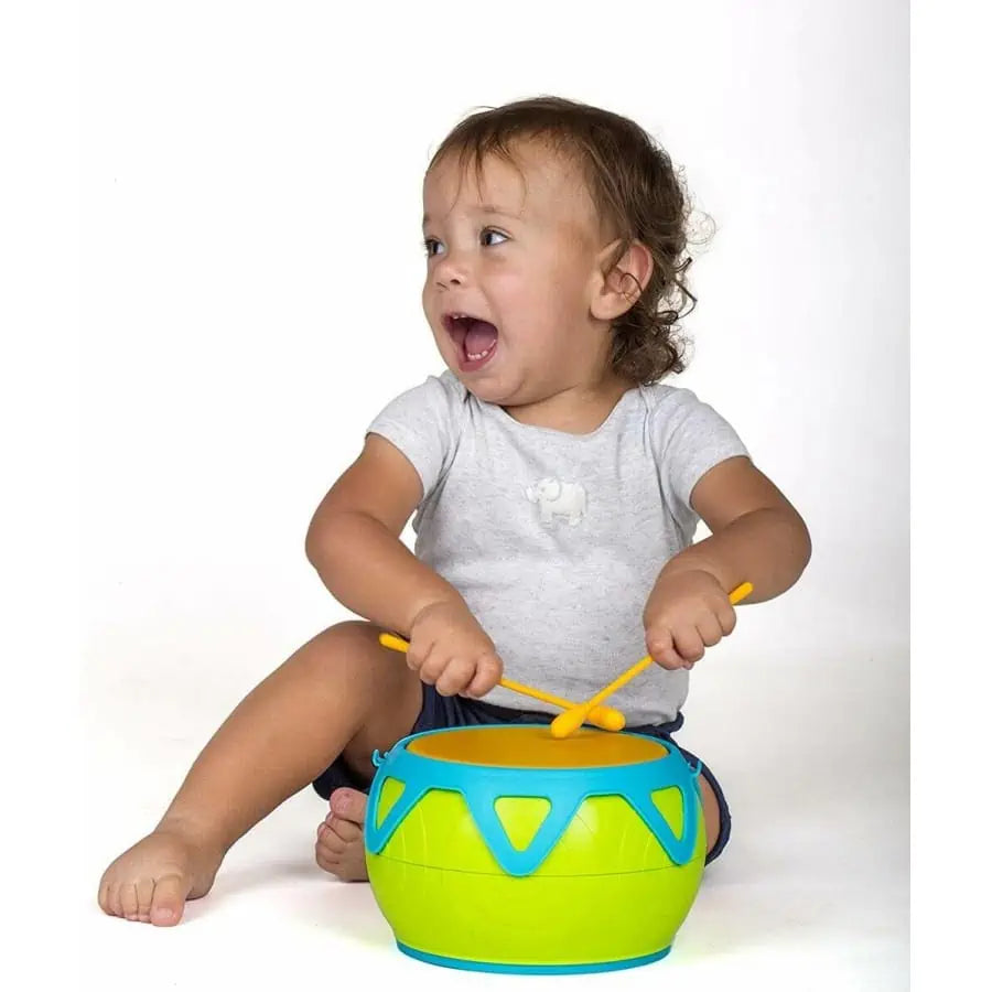 Bebé sentado a tocar o Super Tambor Halilit, olhando para o lado com a boca aberta, demonstrando entusiasmo com o som.