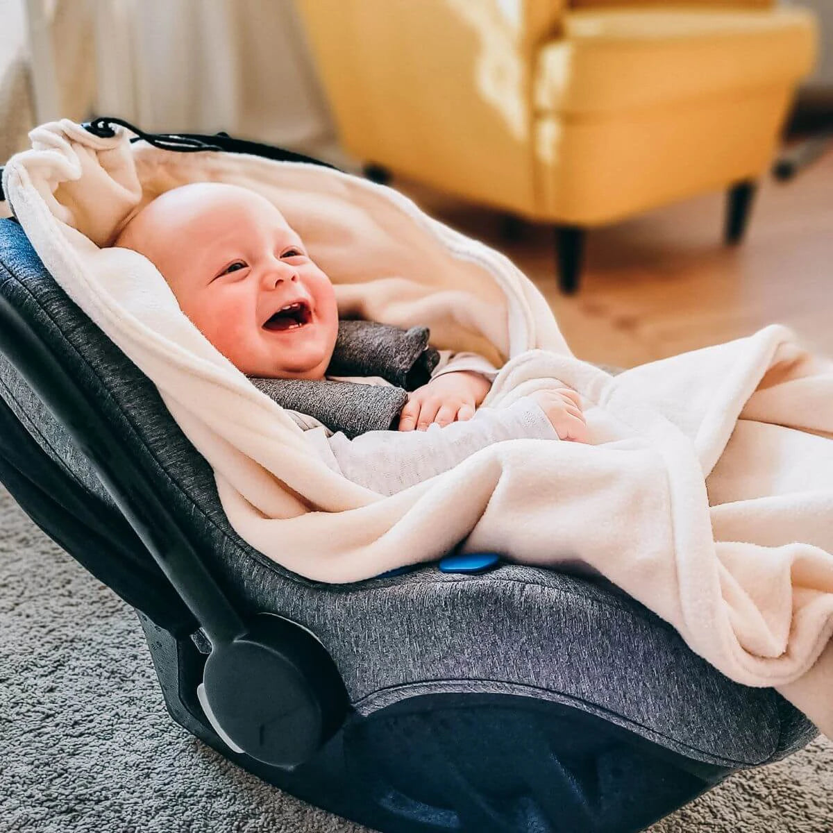 Manta Hoppediz creme dobrada, com o cordão integrado puxado para formar um capuz para o bebé.