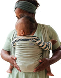 Mãe com turbante verde a usar o pano tecido Hoppediz T6 ELBA, segurando um bebé de costas com padrão às riscas.
