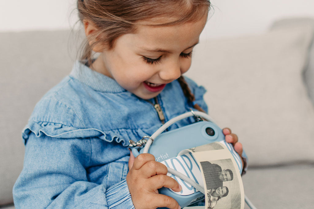 Criança pequena sorridente a observar atentamente a impressão a preto e branco da câmara digital Hoppstar Artist azul.