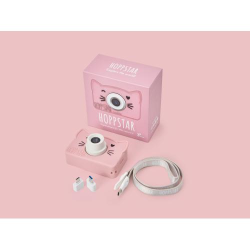 Apresentação da câmara Hoppstar Rookie, caixa e acessórios (cordão, adaptadores) sobre fundo rosa suave.