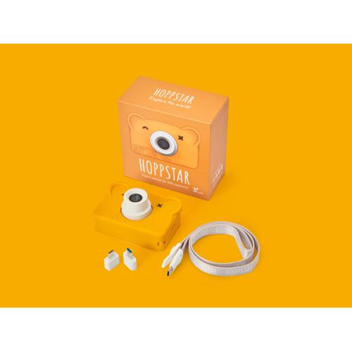 Conteúdo completo da embalagem da Hoppstar Rookie Honey: câmara amarela com capa de silicone, caixa, cordão 2 em 1 e adaptadores, sobre fundo amarelo.