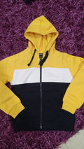Casaco de criança Hublot com fecho, blocos de cor amarelo, branco e azul escuro, e capuz integrado. Vista frontal.
