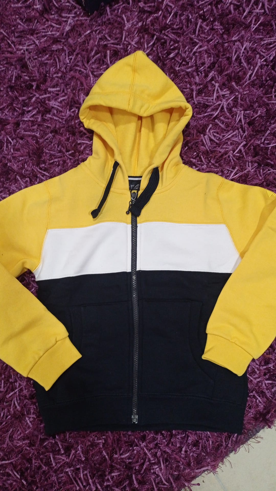 Casaco de criança Hublot com fecho, blocos de cor amarelo, branco e azul escuro, e capuz integrado. Vista frontal.