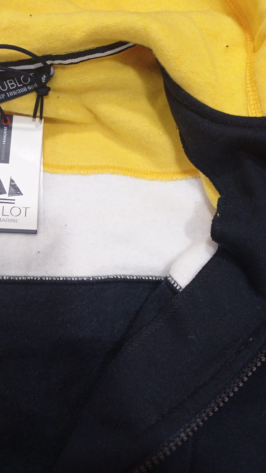 Detalhe do fecho de correr e do tecido canelado do casaco Hublot para criança, em amarelo e azul.
