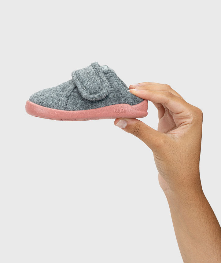 Mão a segurar a pantufa barefoot Igor HOMIE cinza/rosa, evidenciando o material de feltro e a sola flexível.