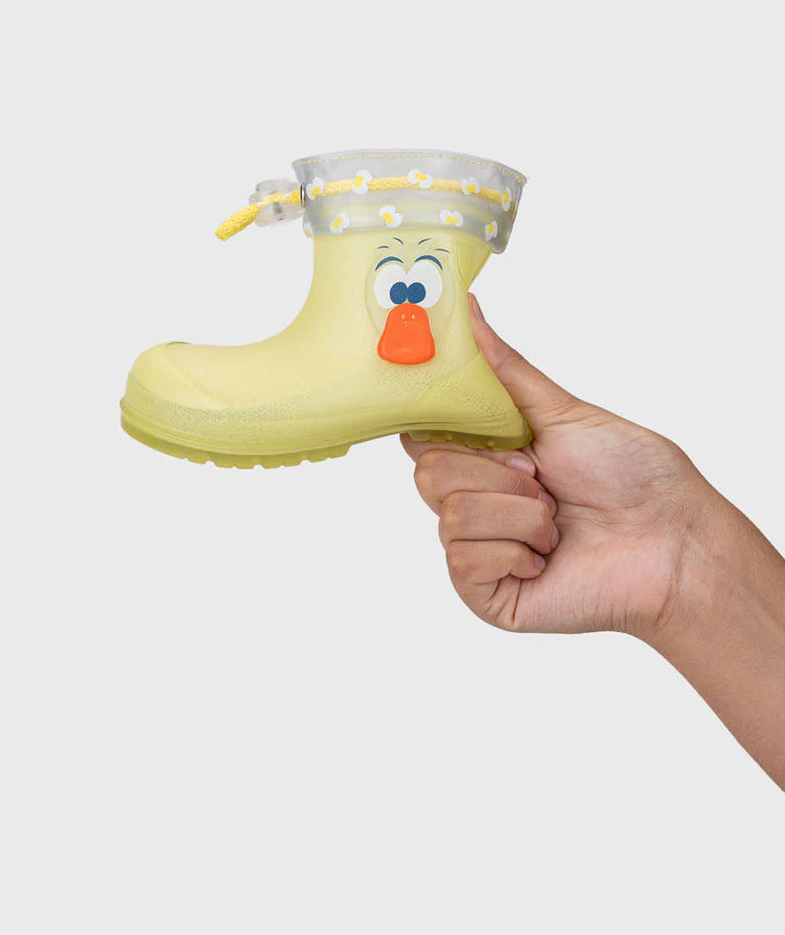 Mão a segurar uma galocha infantil Igor MENDI amarela com decoração de pato, mostrando o tamanho e o topo ajustável.