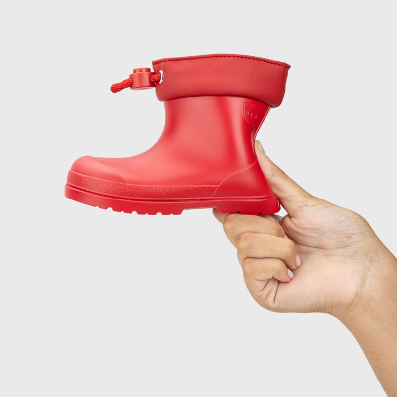 Mão a segurar uma única galocha Igor MENDI vermelha, mostrando o detalhe do fecho ajustável em cordão vermelho na parte superior do cano.