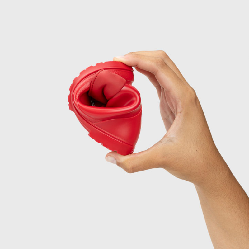 Uma mão segura uma galocha Igor vermelha, dobrada ao meio para demonstrar a extrema flexibilidade e maleabilidade do material de borracha.