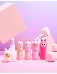 Cinco bálsamos labiais Inuwet Bunny de diferentes tons de rosa e pêssego, com um aberto, num cenário divertido com marshmallows.