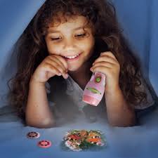 Criança sorridente a usar a lanterna projetora cor-de-rosa no escuro, projetando imagens de animais no chão à sua frente.